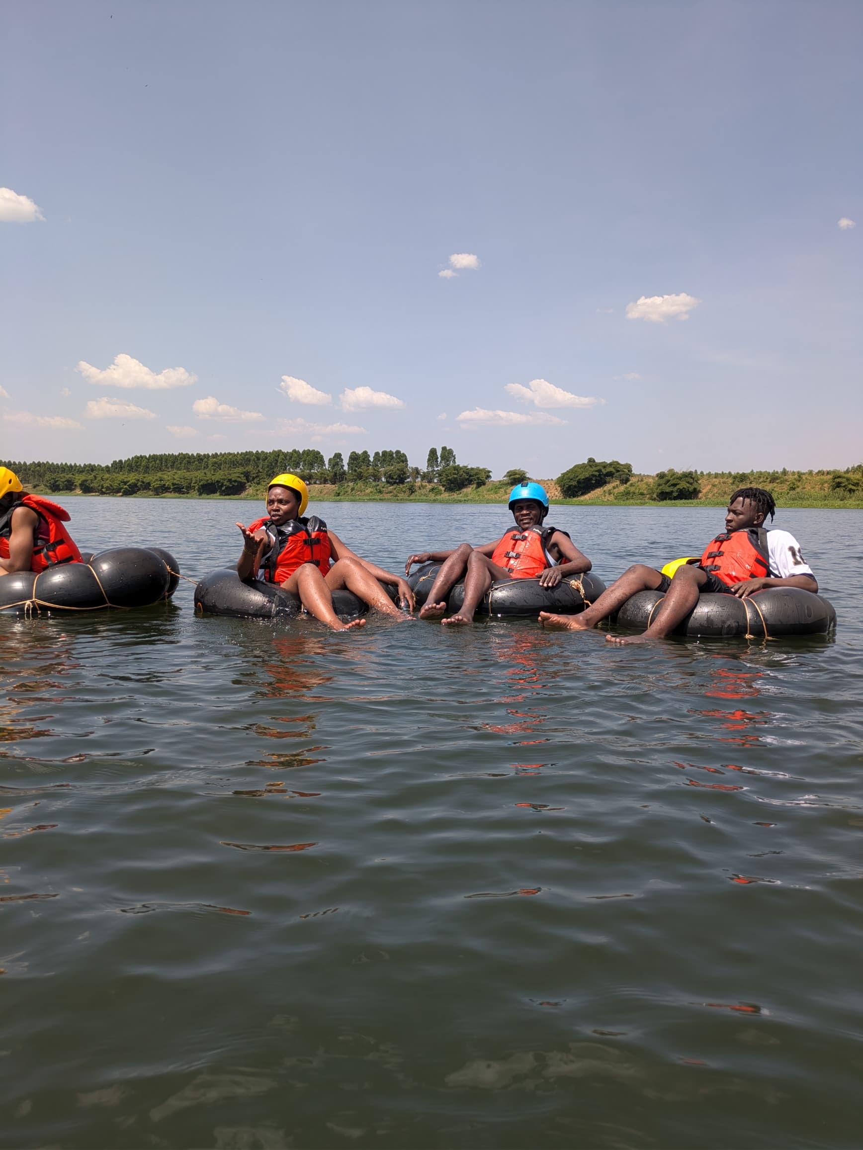 Group of five floating the flat Nile on tubes, red life vests, bright sky